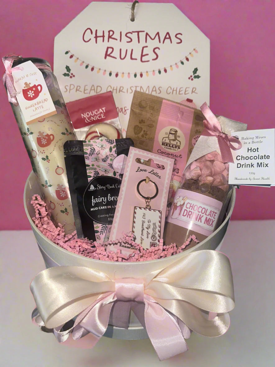 Gift basket with various items including hot chocolate drink mix and nougat, against a pink background with 'Christmas Rules' sign.